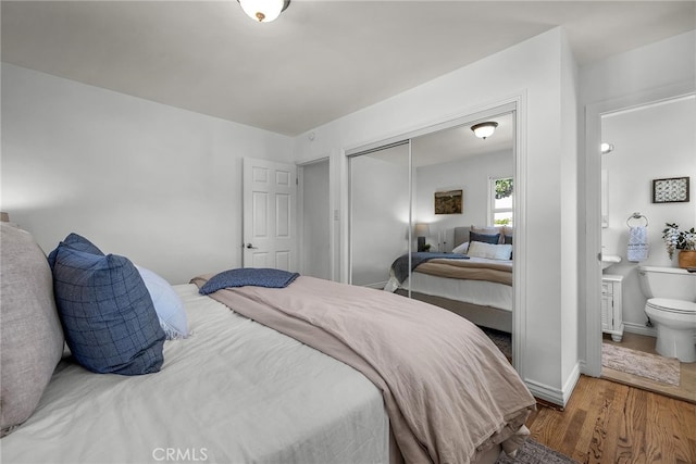 bedroom with baseboards, a closet, wood finished floors, and connected bathroom