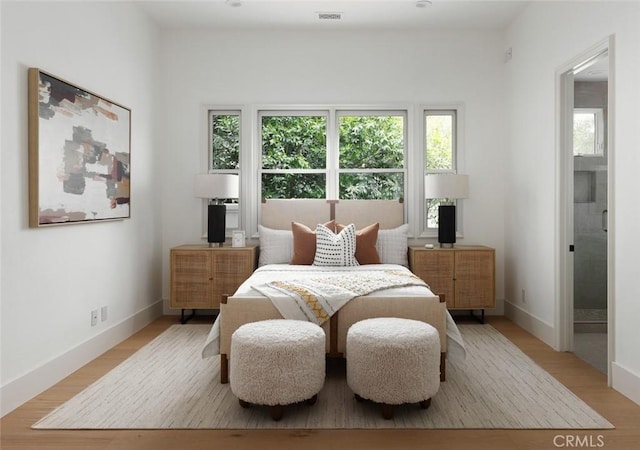 bedroom featuring ensuite bath, light wood-style flooring, visible vents, and baseboards