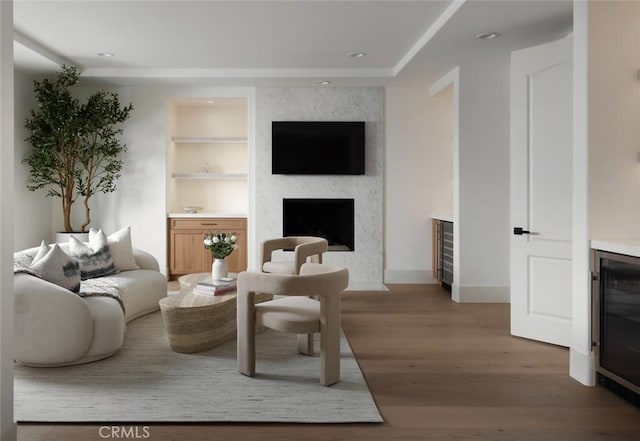 living room with built in shelves, wine cooler, a premium fireplace, light wood-type flooring, and baseboards