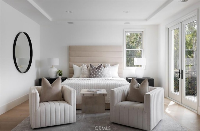 bedroom featuring access to outside, wood finished floors, and a raised ceiling