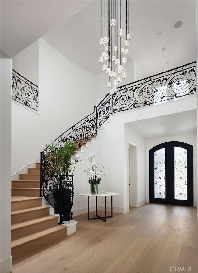 foyer entrance featuring arched walkways, wood finished floors, a towering ceiling, french doors, and stairway