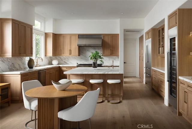 kitchen with a center island, wall chimney exhaust hood, a kitchen breakfast bar, light wood-type flooring, and tasteful backsplash