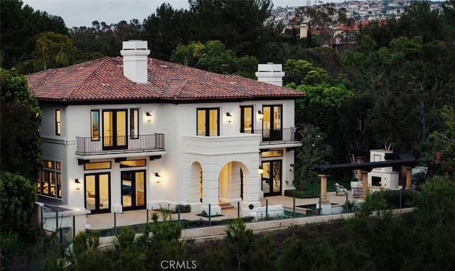 back of house with a patio, a chimney, french doors, and a balcony