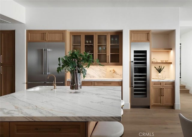 kitchen with wine cooler, high quality fridge, glass insert cabinets, light wood-style floors, and a sink