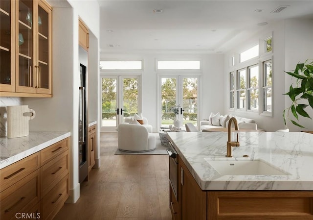 kitchen with french doors, a sink, open floor plan, wood finished floors, and brown cabinets