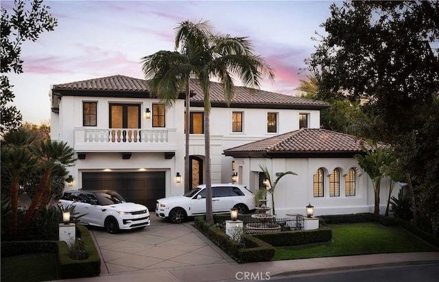 mediterranean / spanish-style home featuring a tile roof, stucco siding, a balcony, a garage, and driveway