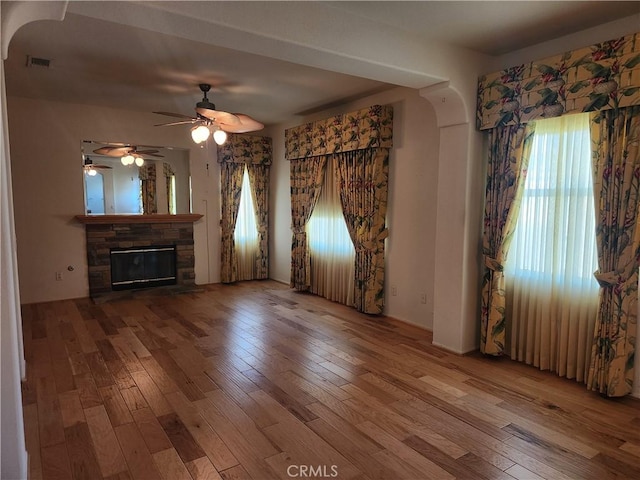 unfurnished living room with visible vents, arched walkways, wood finished floors, and a stone fireplace