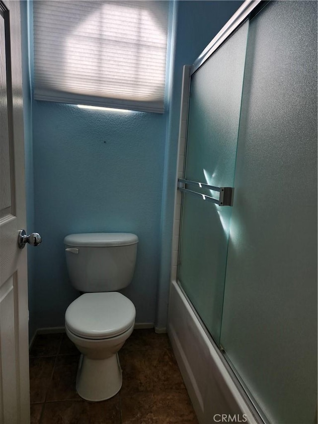 bathroom featuring toilet, shower / bath combination with glass door, tile patterned flooring, and baseboards