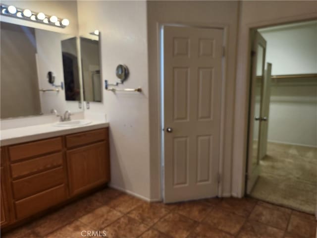 full bath featuring a walk in closet, vanity, and baseboards