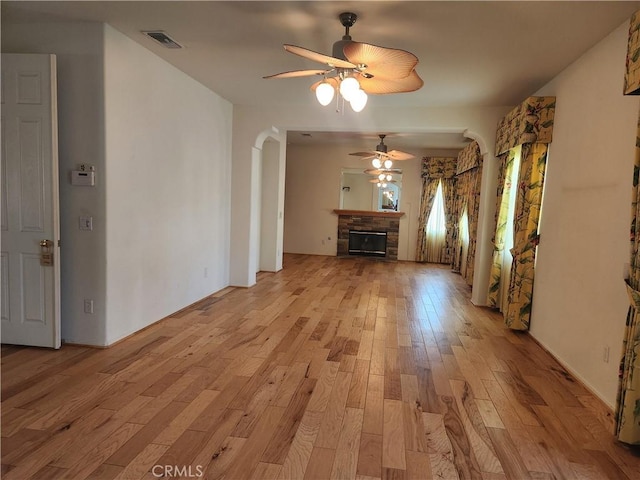 unfurnished living room with arched walkways, a fireplace, light wood finished floors, visible vents, and ceiling fan