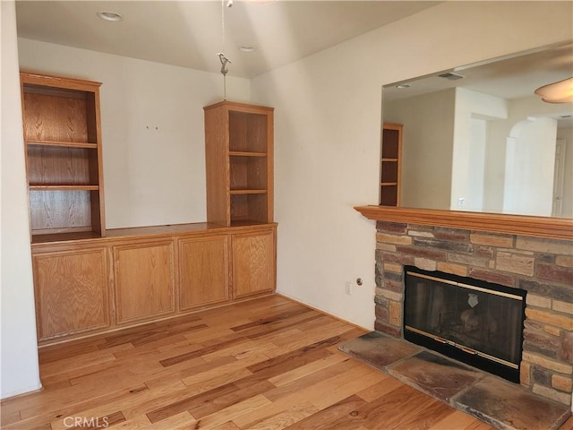 unfurnished living room featuring light wood finished floors and a stone fireplace