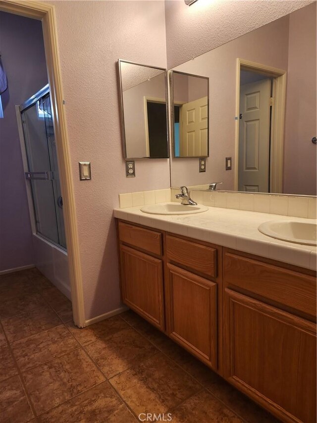 bathroom featuring enclosed tub / shower combo, double vanity, a sink, and baseboards