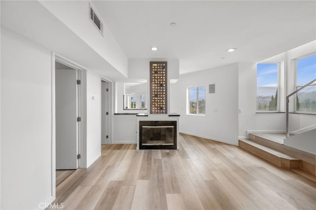 unfurnished living room featuring light wood-style flooring, visible vents, baseboards, and a glass covered fireplace