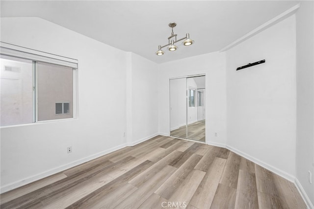 empty room with a notable chandelier, wood finished floors, visible vents, and baseboards