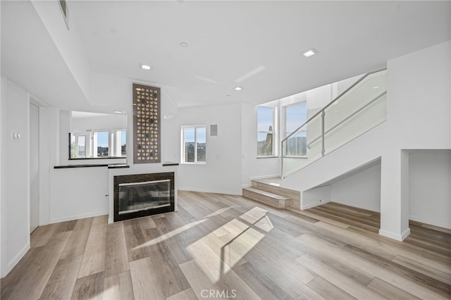 living room with stairs, baseboards, wood finished floors, and a glass covered fireplace