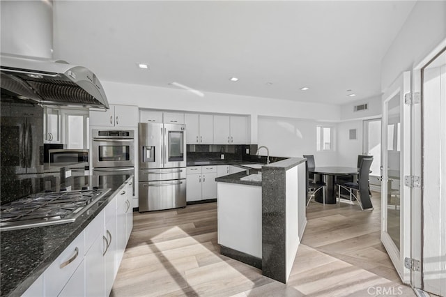 kitchen featuring a peninsula, exhaust hood, visible vents, light wood-style floors, and appliances with stainless steel finishes