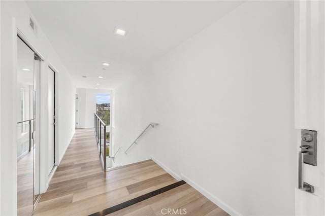 hallway featuring light wood-type flooring, baseboards, and an upstairs landing