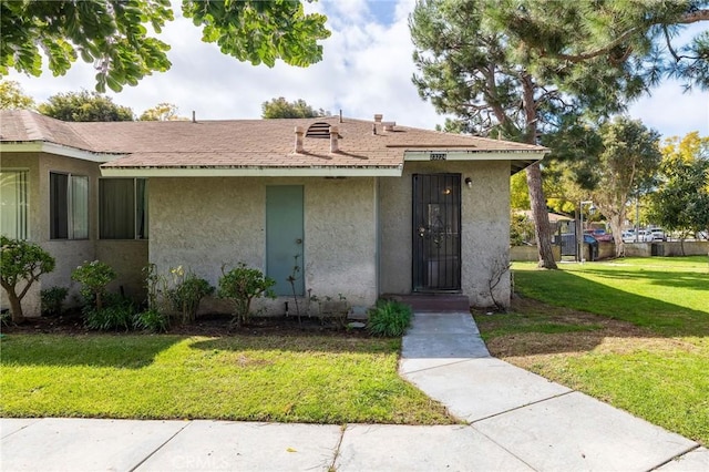 view of front facade featuring a shingled roof, a front yard, and stucco siding