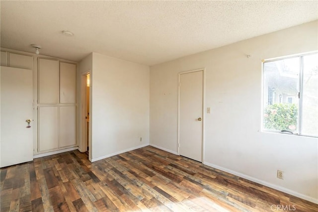 empty room featuring a textured ceiling, wood finished floors, and baseboards