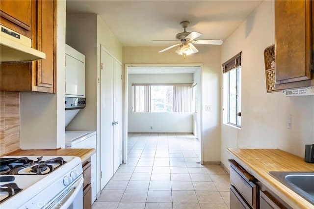 kitchen with gas range gas stove, light tile patterned floors, stacked washer and dryer, brown cabinetry, and under cabinet range hood