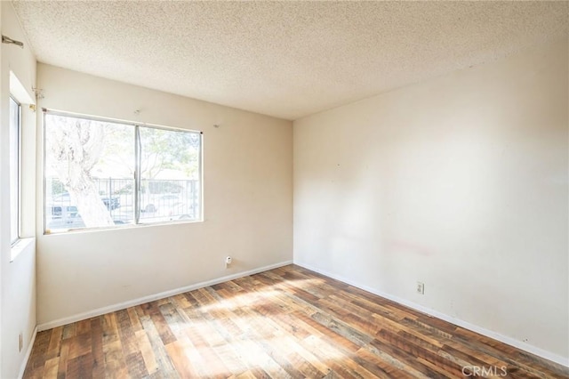 spare room with a textured ceiling, wood finished floors, and baseboards