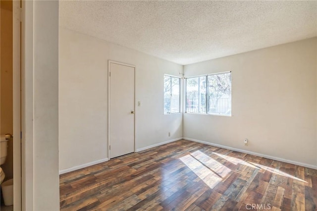 empty room featuring a textured ceiling, baseboards, and wood finished floors