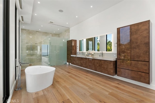 full bath with double vanity, a stall shower, a soaking tub, and wood finished floors