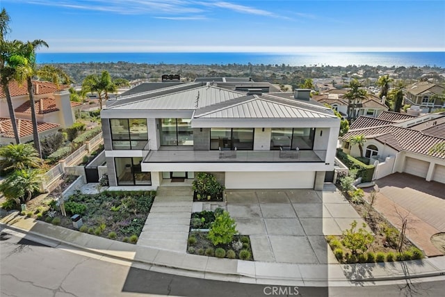 contemporary house with metal roof, a balcony, a garage, concrete driveway, and a standing seam roof