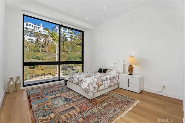 bedroom featuring a wall of windows, recessed lighting, baseboards, and wood finished floors