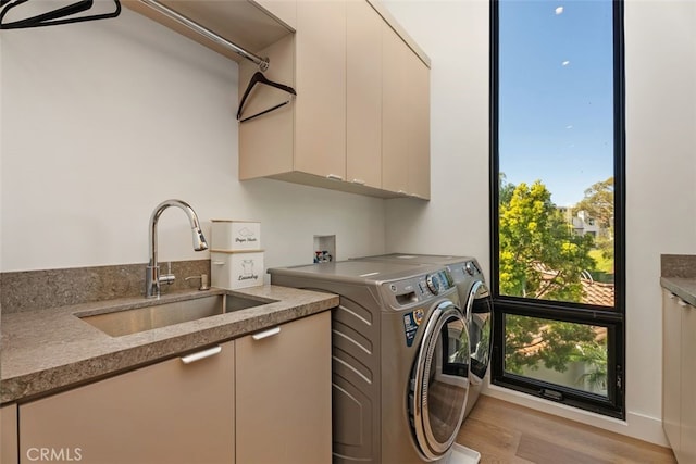 clothes washing area featuring cabinet space, a sink, washing machine and clothes dryer, and wood finished floors