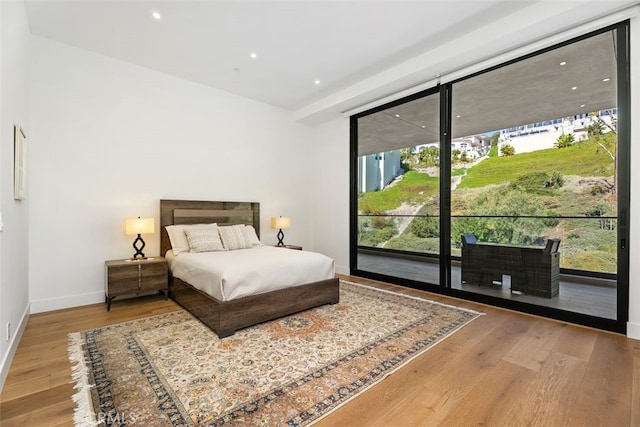 bedroom with access to exterior, recessed lighting, expansive windows, wood finished floors, and baseboards