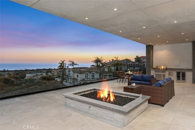 patio terrace at dusk with beverage cooler, area for grilling, an outdoor living space with a fire pit, and a grill