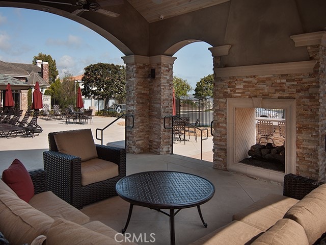 view of patio / terrace with ceiling fan, an outdoor living space with a fireplace, and fence