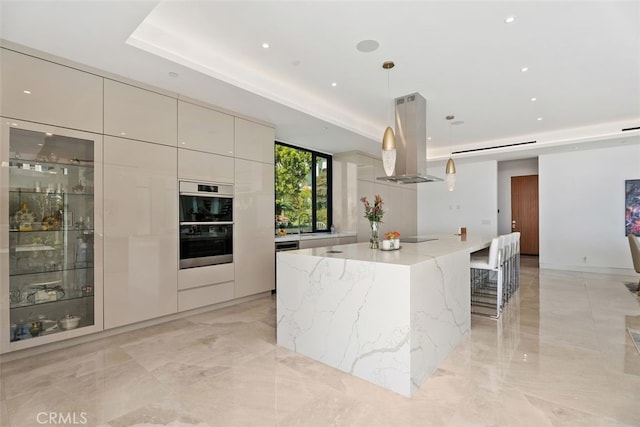 kitchen with light stone counters, island range hood, a spacious island, modern cabinets, and a raised ceiling