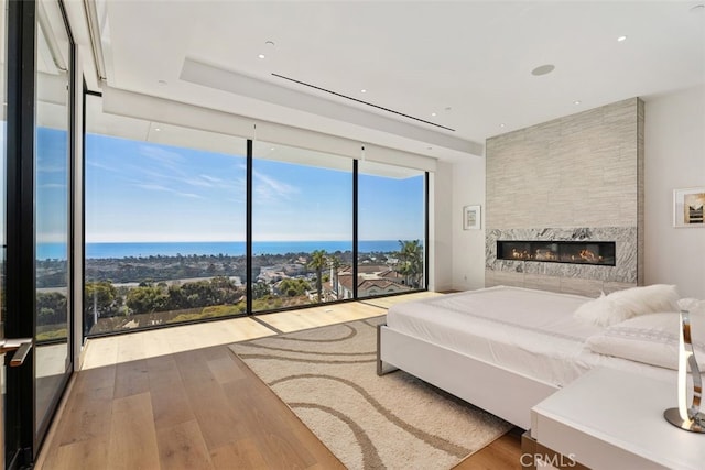 unfurnished bedroom featuring a wall of windows, a premium fireplace, a water view, and wood finished floors