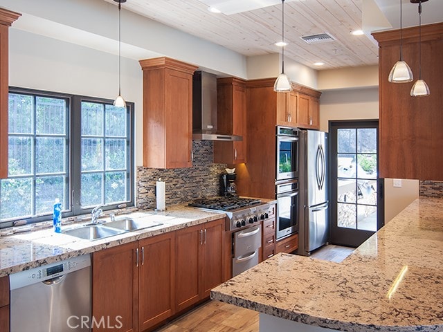 kitchen featuring visible vents, brown cabinetry, appliances with stainless steel finishes, wall chimney range hood, and a sink