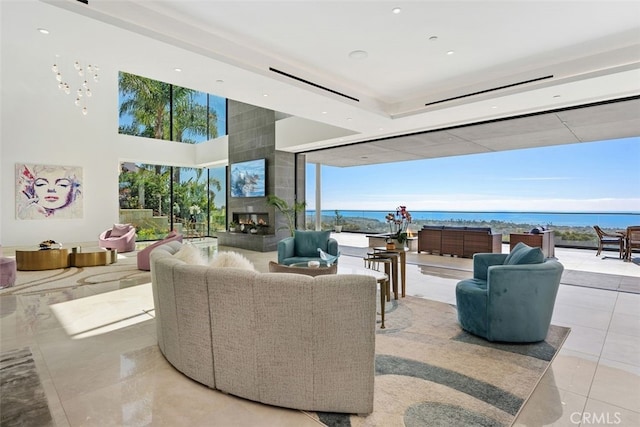 living room with a large fireplace, a water view, tile patterned flooring, expansive windows, and a high ceiling