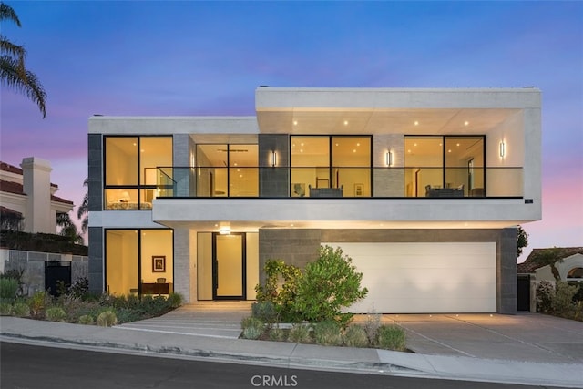 modern home featuring stucco siding, a balcony, concrete driveway, and an attached garage