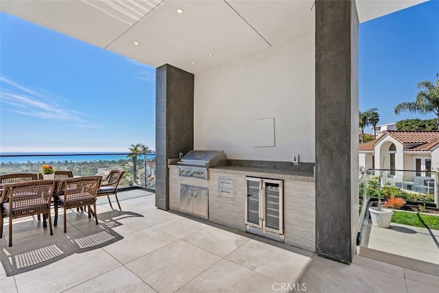 view of patio / terrace with beverage cooler, a water view, a grill, outdoor dining area, and exterior kitchen