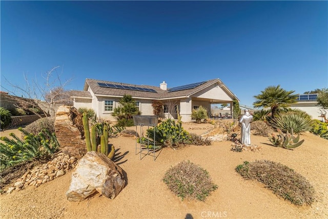 ranch-style home featuring solar panels, a chimney, fence, and stucco siding