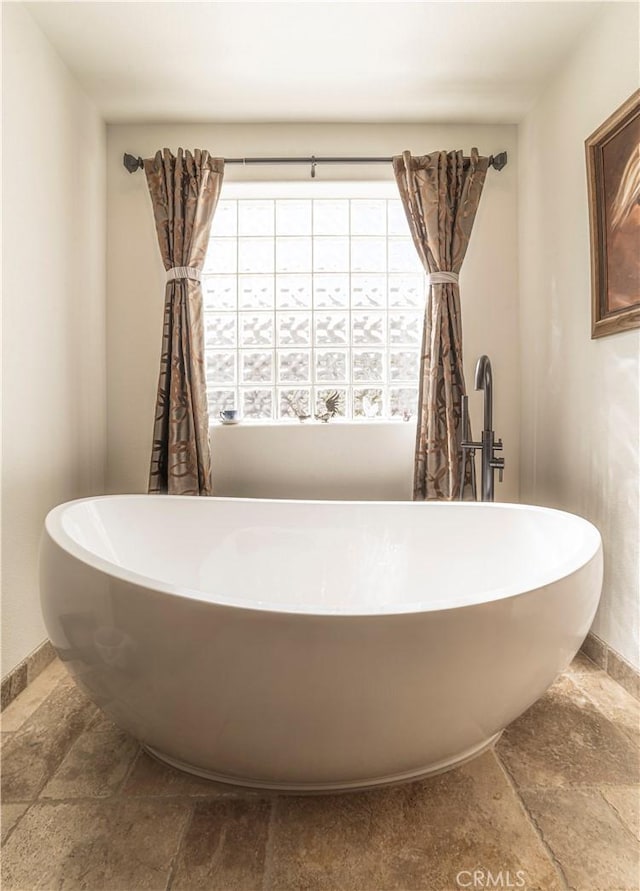 bathroom with a freestanding bath, stone finish floor, and baseboards