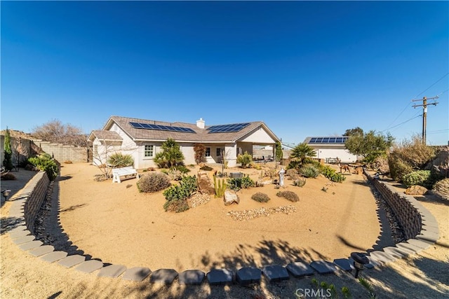 rear view of house with a chimney, fence private yard, and roof mounted solar panels