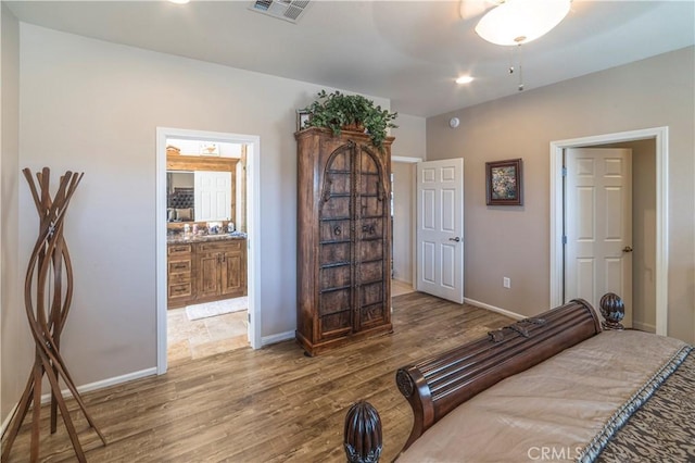 bedroom with visible vents, ensuite bathroom, baseboards, and wood finished floors