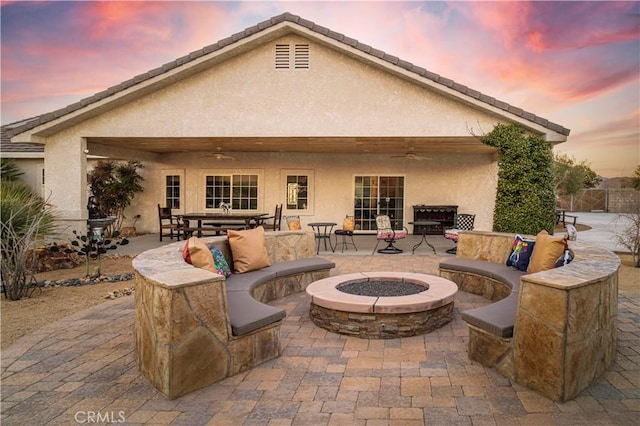 rear view of property featuring an outdoor living space with a fire pit, ceiling fan, a patio, and stucco siding