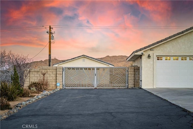 garage at dusk featuring driveway, a gate, and fence