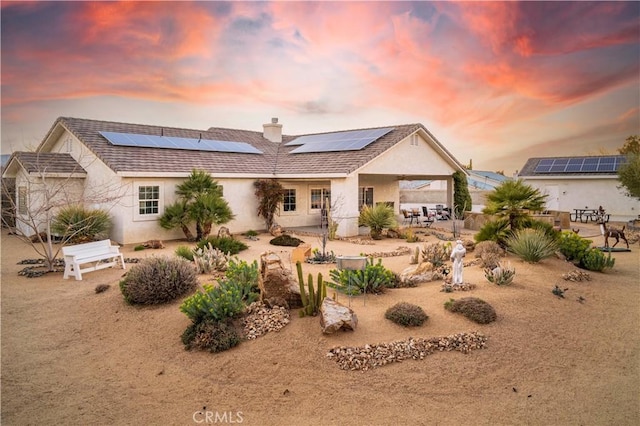 back of house featuring solar panels, a patio, a chimney, and stucco siding