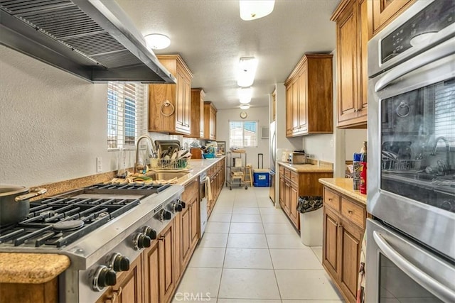 kitchen featuring light tile patterned flooring, stainless steel appliances, a sink, light countertops, and wall chimney exhaust hood