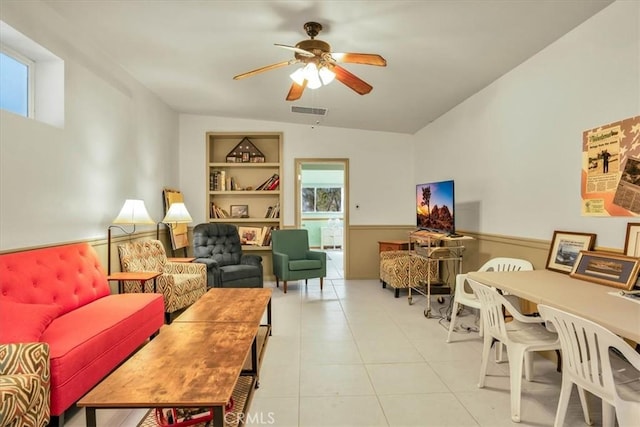 living area with built in features, a wainscoted wall, light tile patterned floors, visible vents, and a ceiling fan