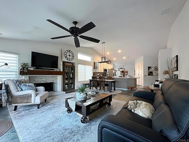 living area featuring a ceiling fan, vaulted ceiling, and a stone fireplace