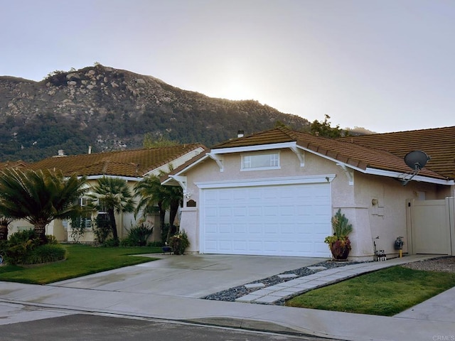 view of front of property with stucco siding, an attached garage, a front yard, a mountain view, and driveway